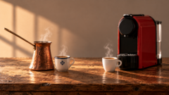 Una vecchia cuccuma di rame e una moderna macchina da caffè, ciascuna accanto alla propria tazza fumante.